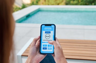 Woman using an application on her smartphone to control the swimming pool temperature like the olympics