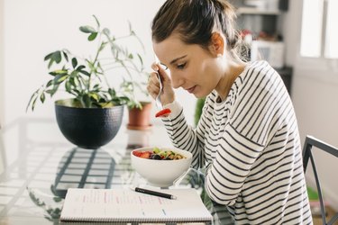 woman eating breakfast while looking at papers