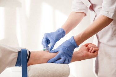 a close up of a nurse wearing blue surgical gloves drawing blood from a patient