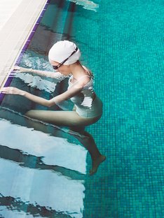 Woman starting to swim in a pool wearing goggles and swim cap