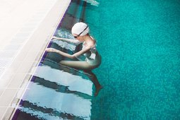 Woman starting to swim in a pool wearing goggles and swim cap