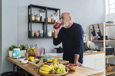 Older adult drinking a protein smoothie to gain weight, standing next to a bowl of bananas and fruit in their kitchen