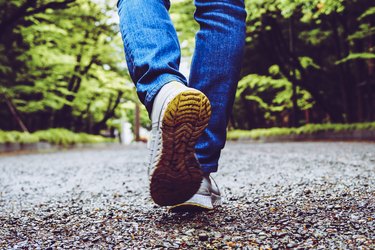 Close view of person wearing walking shoes walking on a gravel path in the woods