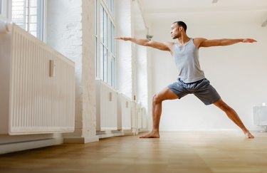 Young person in a grey tank top and shorts practicing yoga for knee pain in a white yoga studio with wood floors