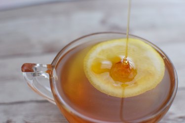a close up of honey being poured over a slice of lemon in a glass teacup