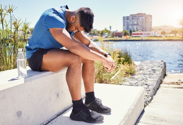 Person wearing blue T-shirt, black shorts and sneakers sitting outside after running needing a sports psychologist