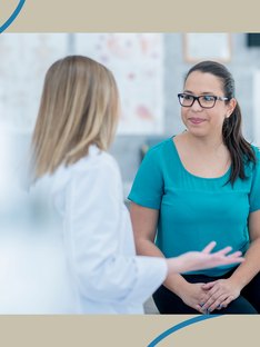 woman in teal t-shirt and glasses speaking with female doctor about PCOS