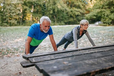older couple doing a incline push-up and core exercises for seniors on a bench in the park